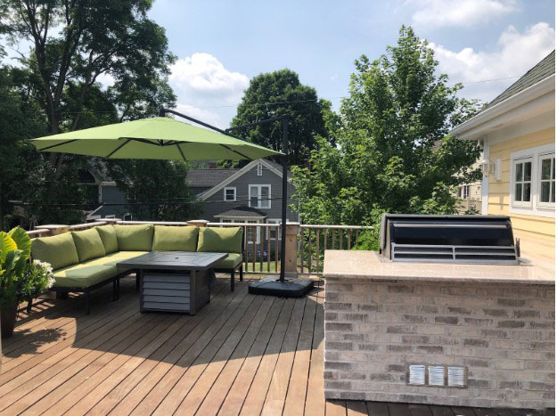 Backyard deck with a sectional green couch, a built in fireplace on the table, and a grilling station