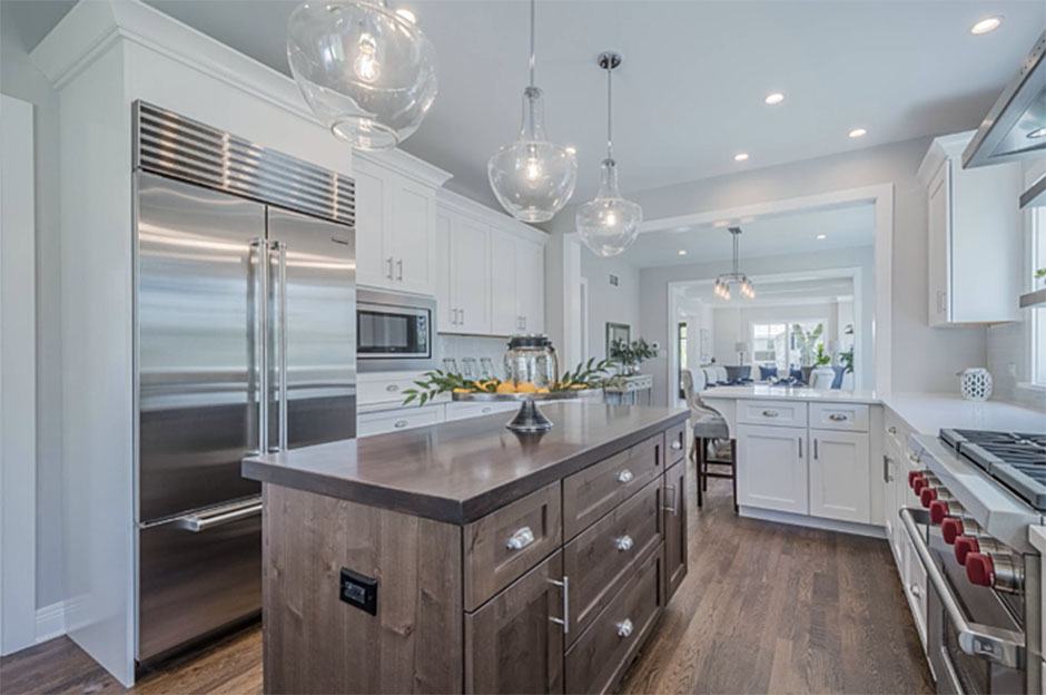 White kitchen with white countertops and a natural wood island with a brown countertop featuring stainless steel appliances