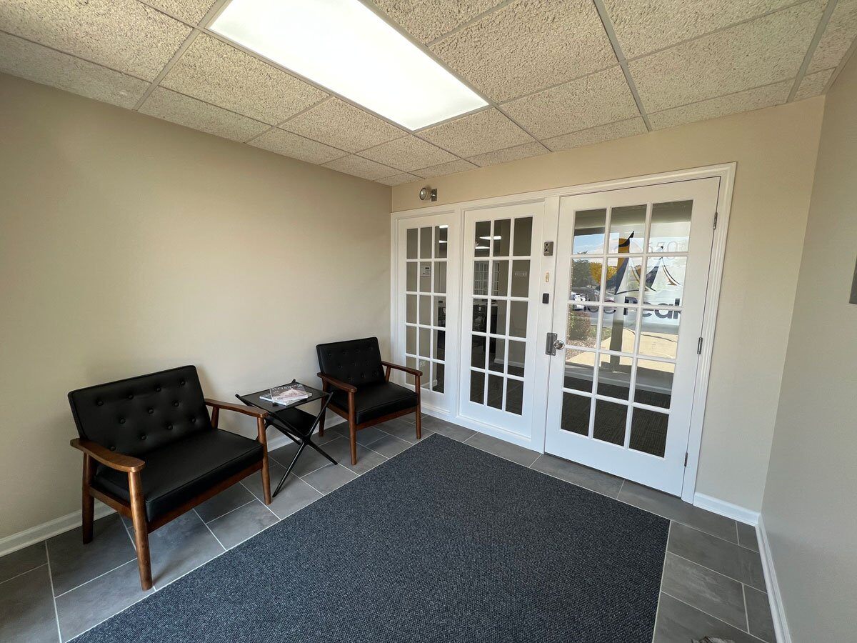 Waiting room with two black wooden chairs on the wall next to a white glass paned door