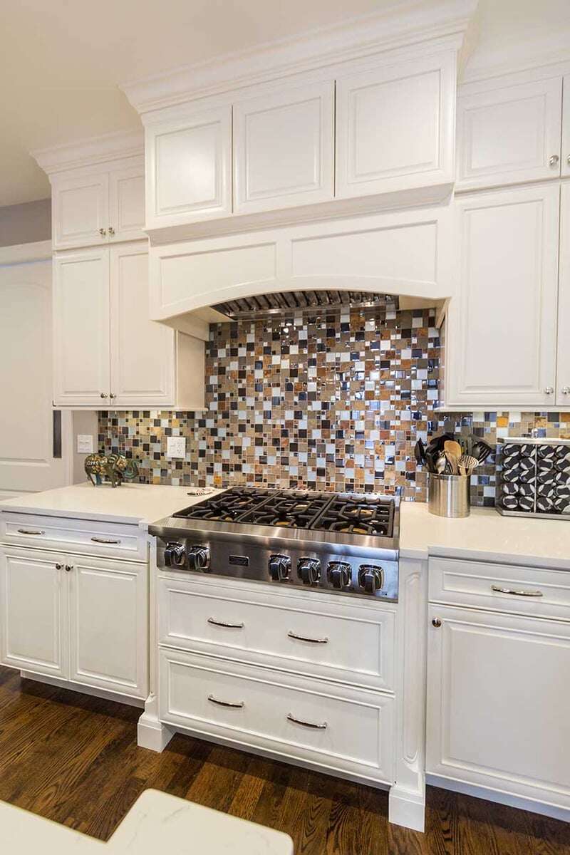 Kitchen over with 6 burner knobs on a gas stovetop with a small block tile backsplash behind it