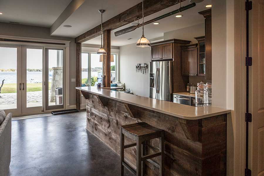 Basement wet bar with a warm and contemporary aesthetic and wood trim. There is also a brown sofa seated in front of the counter