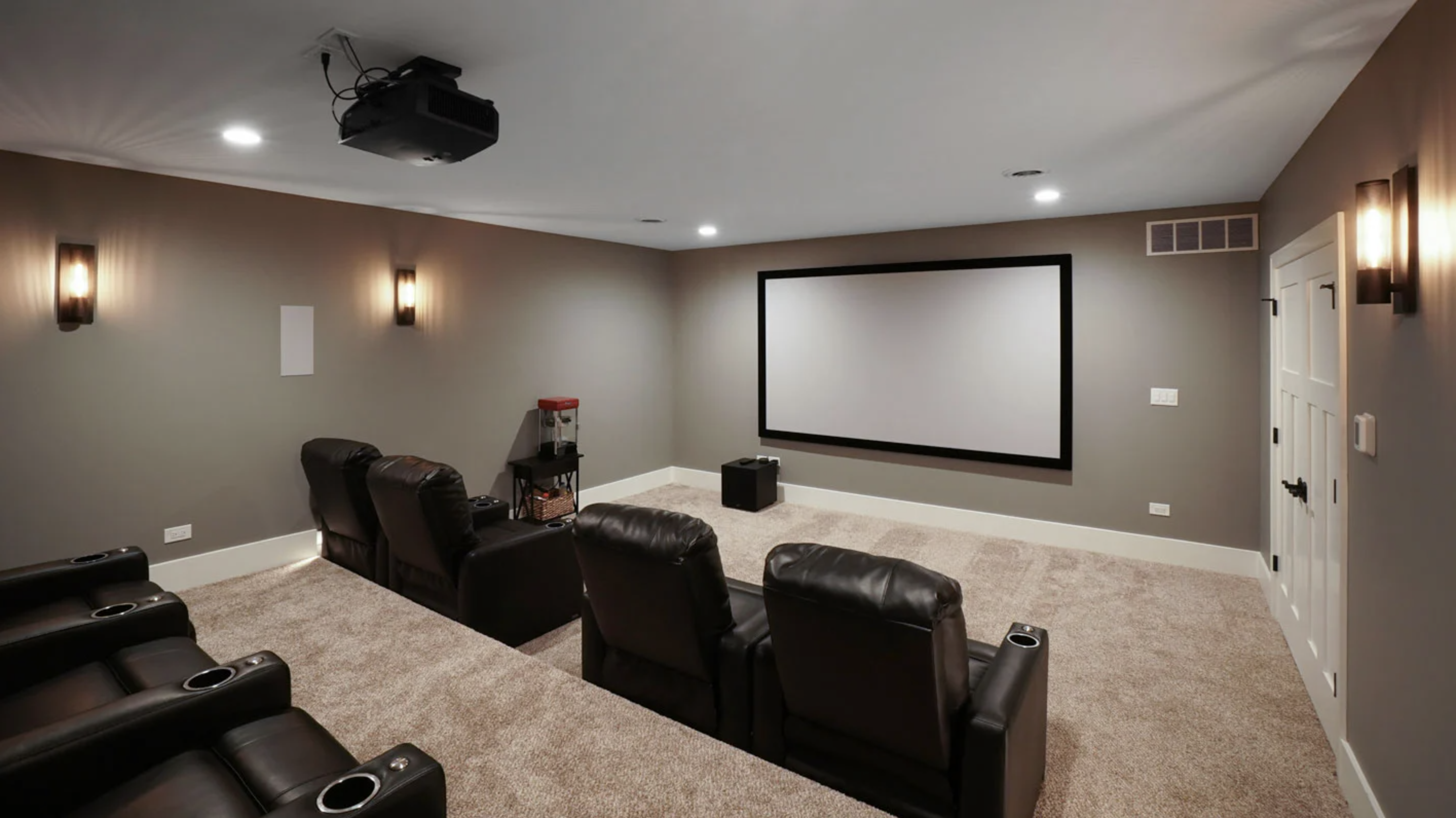 Luxury basement theatre room with black leather recliners and a large projector screen on the wall