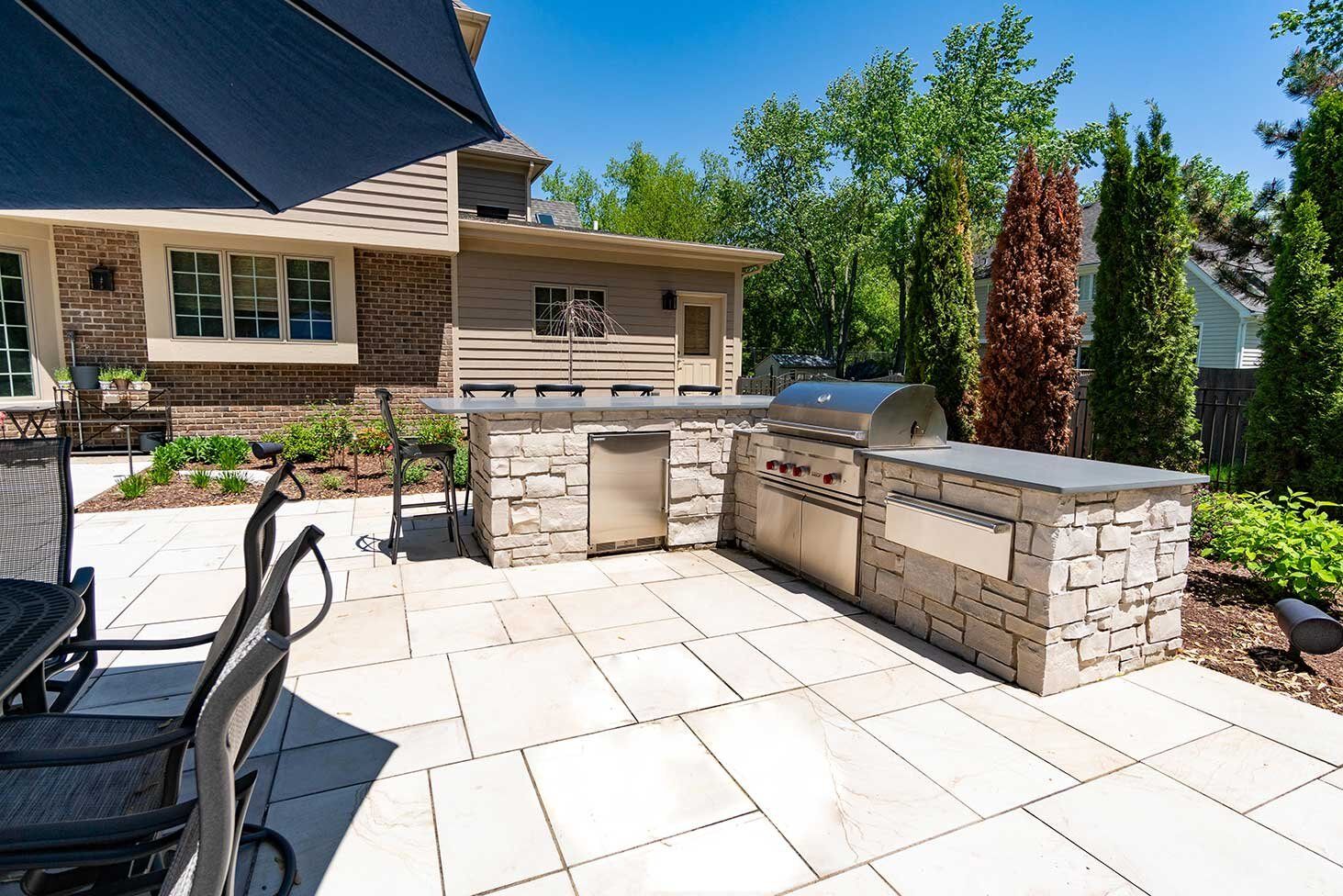 Ourdoor kitchen with a small shaded seating area and a grill/pizza oven built into the prep station