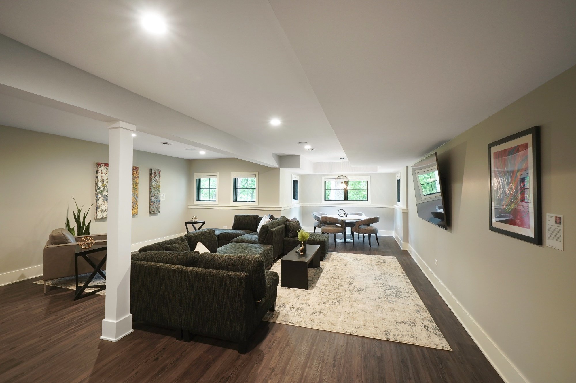 basement with sectional couch, tan area rug, wall mounted television and ceiling can lights